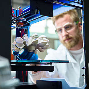Technician inspects a turbine wheel that has just finished printing in a 3D printer.